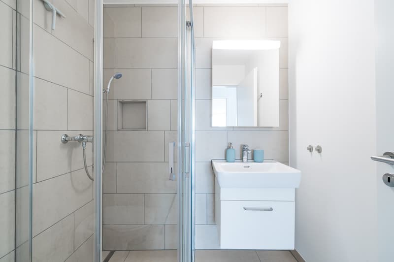 modern bathroom with shower, white sink, mirror, and tiled walls