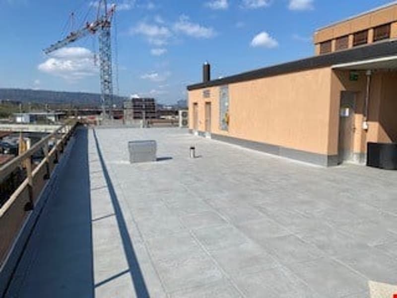 Large open rooftop area with concrete flooring, surrounded by a railing. There is a construction crane visible in the background.
