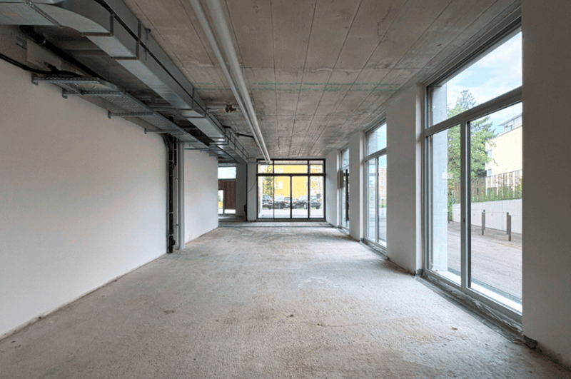 Empty corridor, concrete floor, white walls, ceiling with pipes, multiple glass windows, view of parking lot