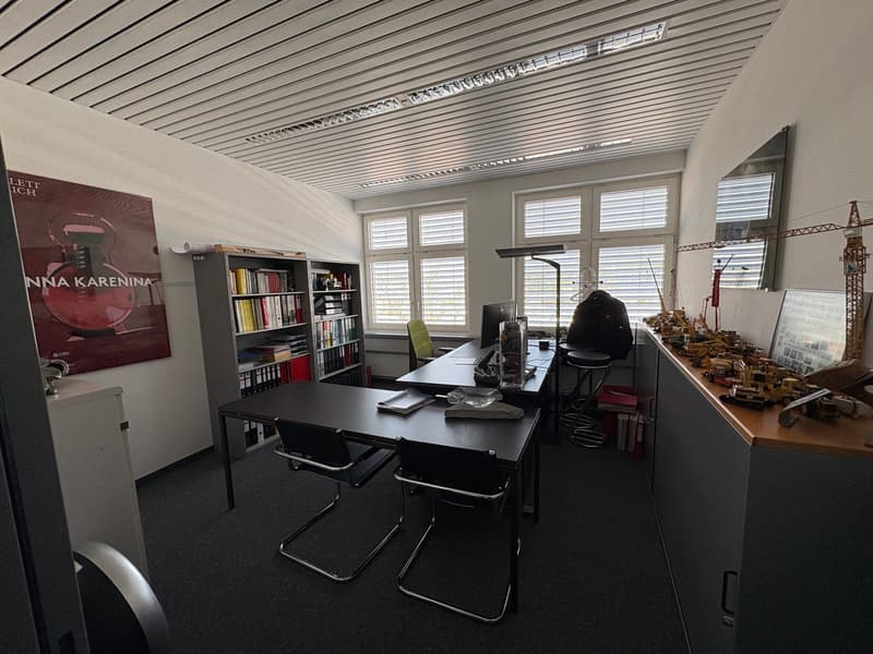 Office room with desks, chairs, bookshelves, and a poster on the wall