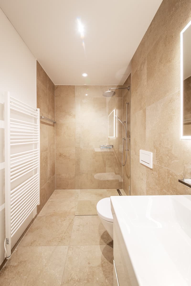 modern bathroom with beige tiles, glass shower enclosure, white toilet, white sink, white towel radiator