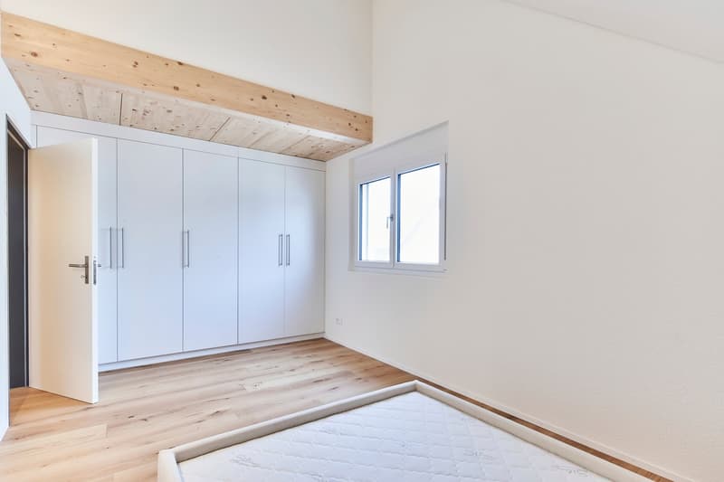 Spacious bedroom with white walls, wooden ceiling, large built-in wardrobes, and hardwood flooring. The room has a window providing natural light.