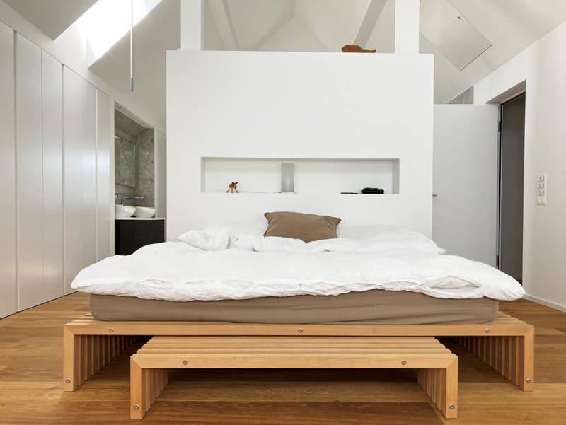 modern bed with wooden frame, light brown sheets, white ceiling, wooden floor, white wall