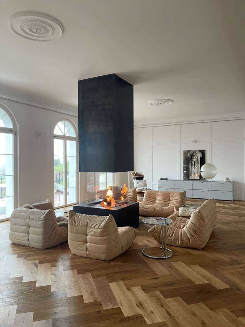 fireplace, wooden floors, beige couches, coffee table, large windows