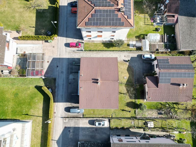 Aerial view of a residential area with multiple houses, solar panels on roofs, and cars parked in driveways.
