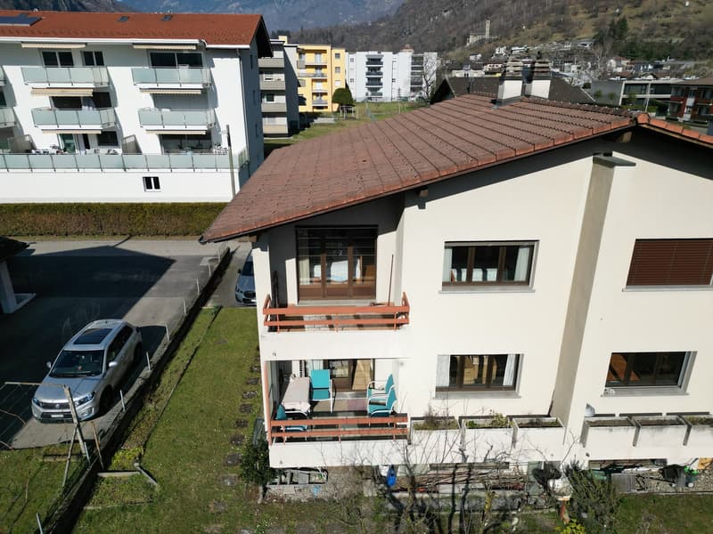 Two-story house, brown roof, white walls, balcony with outdoor furniture, parking area, car parked
