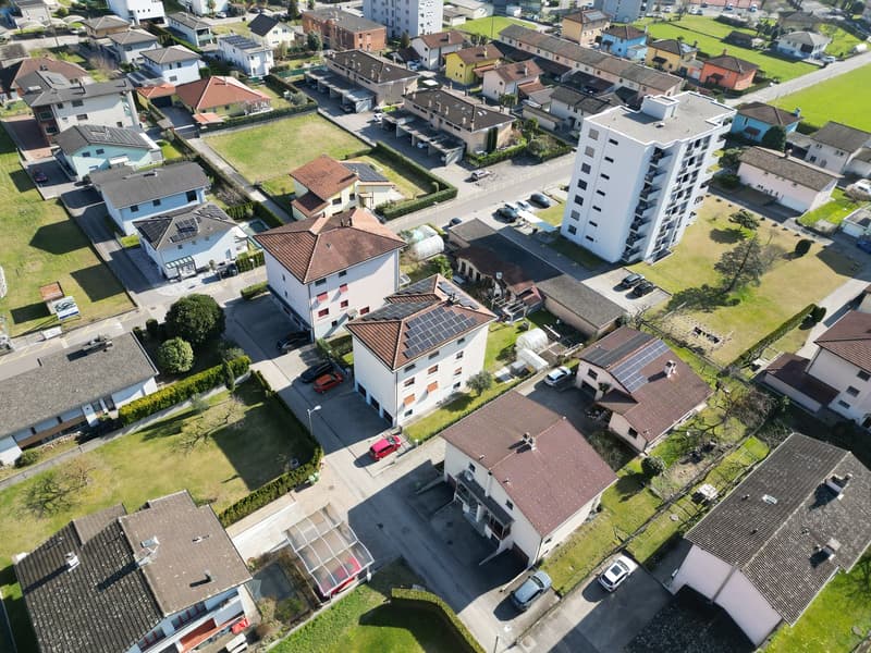 Aerial view of a neighborhood with multiple houses, some with solar panels, and a few cars parked in front of the houses.