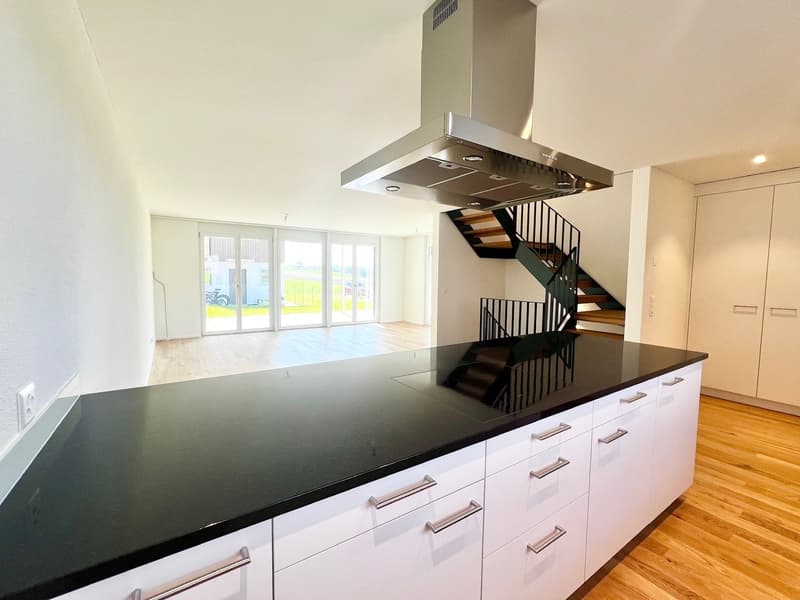 modern kitchen with black granite countertop, white cabinets, stainless steel range hood, wooden floor, large windows, staircase