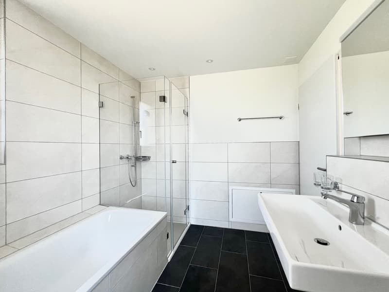 modern bathroom with white tiles, bathtub, shower, sink, mirror, and black tiles on the floor