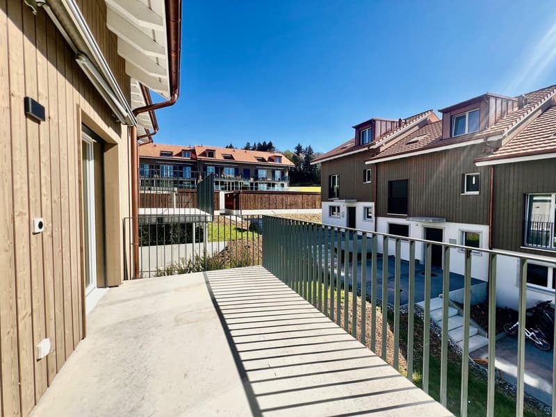 Balcony with metal railings, wooden walls, and a view of other buildings and a grassy area.