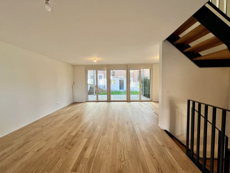 Empty room with wooden floor, white walls, glass sliding doors, staircase, no furniture