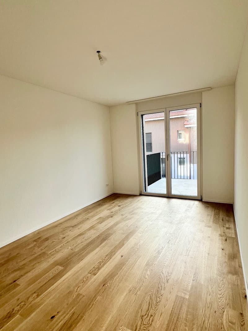 Large room with hardwood floor, white walls, sliding glass door leading to balcony