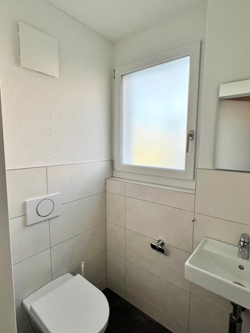 small bathroom with white tiled walls, white toilet, white sink, small window, mirror