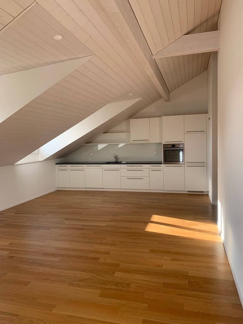Spacious kitchen with white cabinets, wooden floors, and slanted ceiling with exposed beams
