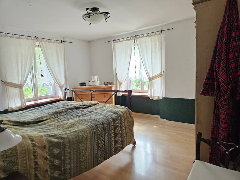 Bedroom with wooden floor, bed, nightstand, wooden cabinet, white curtains, and a window seat