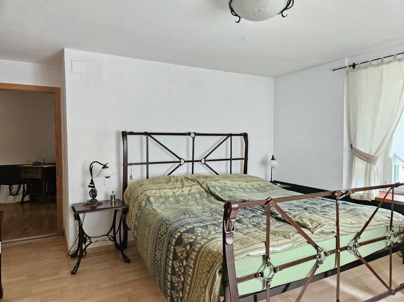 Bedroom with a bed, nightstand, lamp, and a desk in the hallway.