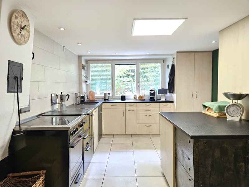 modern kitchen with white tiles, wooden cabinets, black countertops, gas stove, oven, dishwasher, washing machine, coffee machine, scale, window with blinds