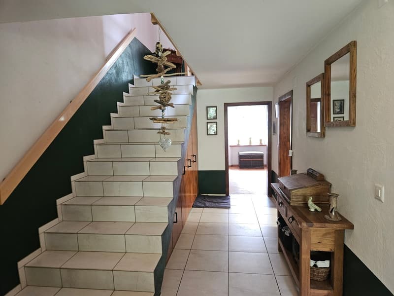 tiled floor, white walls, wooden staircase, wooden desk, mirrors, picture frames, open door, wooden chest, rug