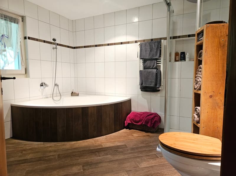 Bathroom with bathtub, shower, toilet, wooden shelves, towels, window with curtain