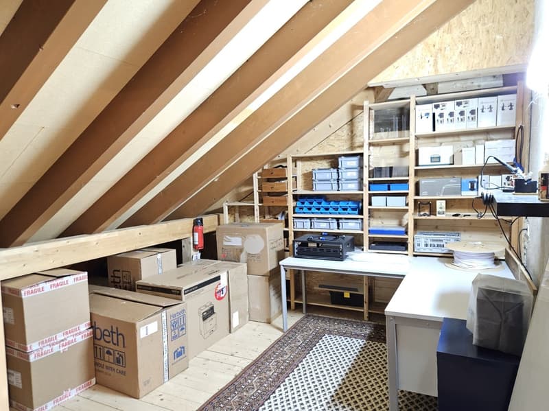 attic room with wooden beams, storage boxes, shelves, desk, and a rug