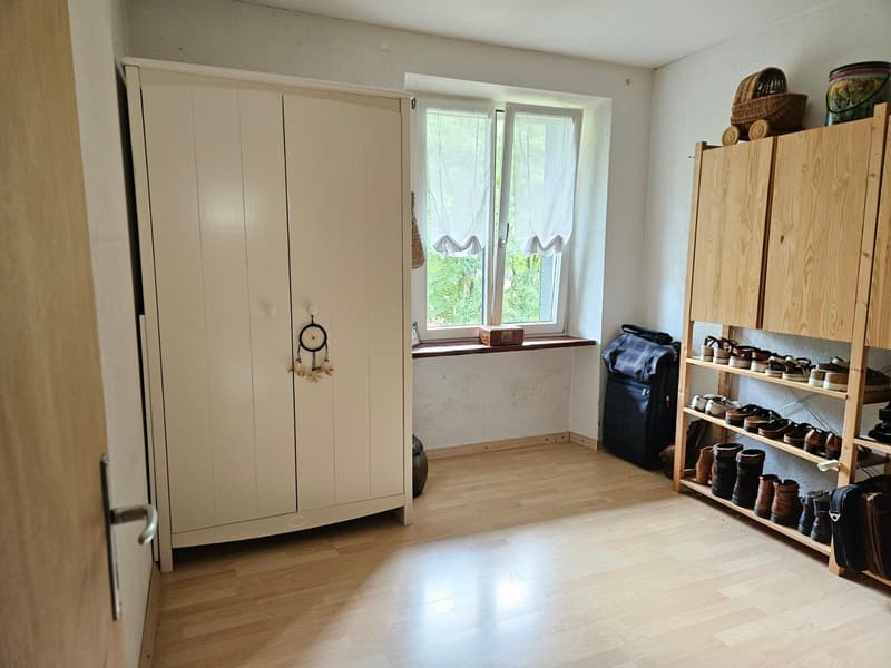 wooden floor, white wardrobe, wooden shoe rack, window with white curtains, storage box on window sill, black suitcase