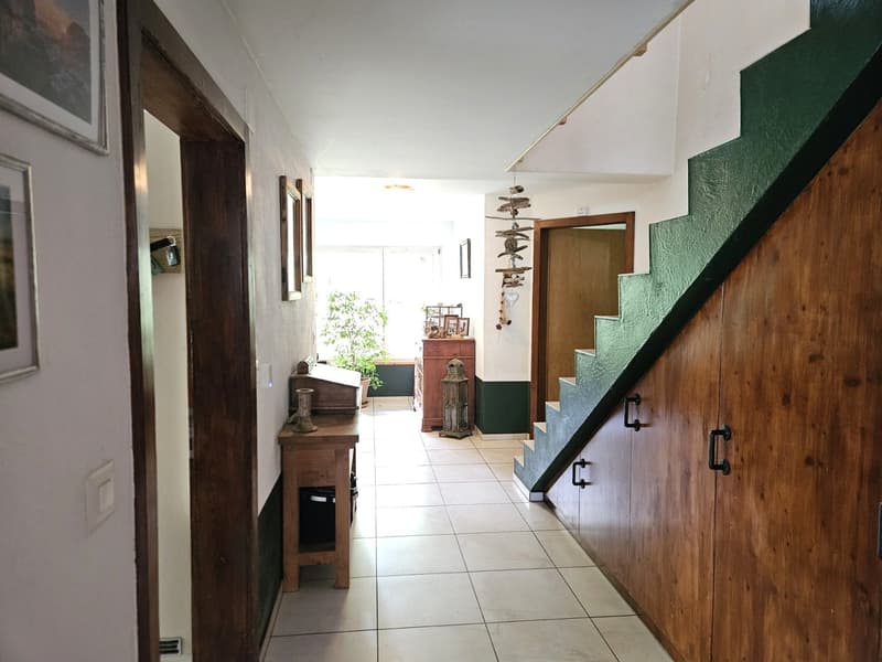white tiled floor, wooden doors, wooden table, green painted staircase, picture frames, potted plant