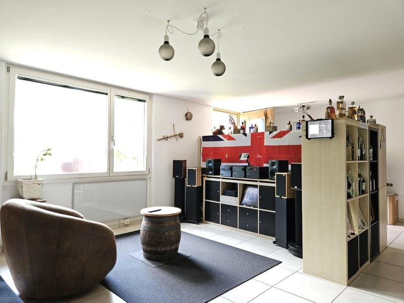 Living room with a couch, a barrel table, a bookshelf, a speaker system, and a window with a plant
