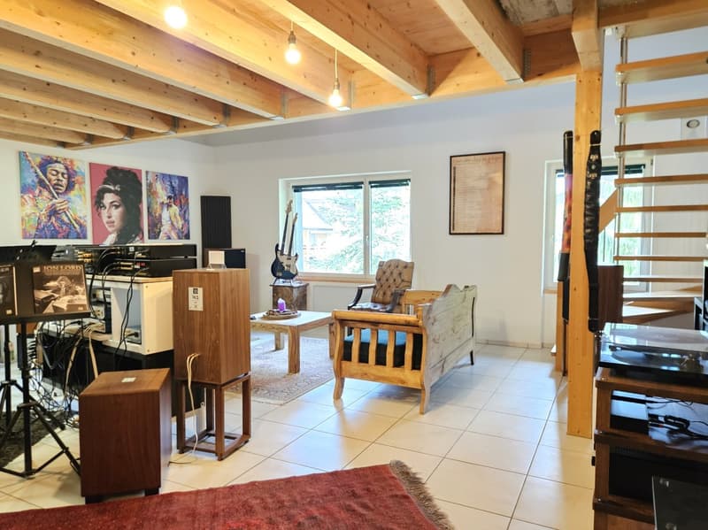 Living room with wooden ceiling, white tiles, wooden couch, wooden table, speakers, guitars, paintings, staircase