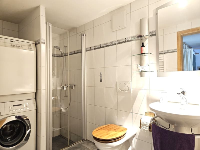white tiled walls, glass shower enclosure, wooden toilet seat, white sink, washing machine, mirror