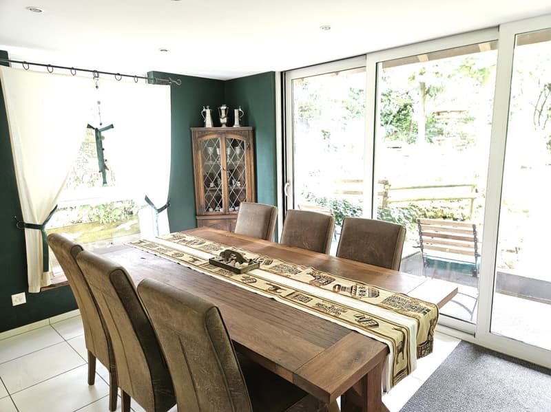 Dining room with wooden table, 6 chairs, green wall, wooden cabinet, sliding glass doors, outdoor bench, garden view