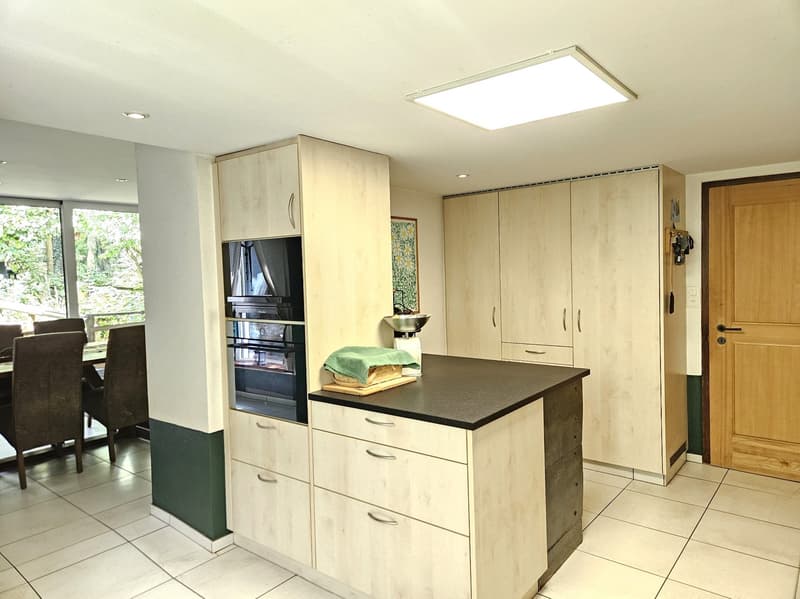 modern kitchen with white tiles, wooden cabinets, black countertop, built-in oven, and a dining area with a table and chairs