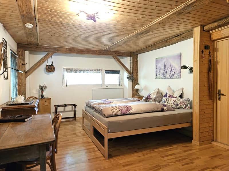 wooden floor, wooden ceiling, bed with storage, desk, chair, lamp, picture, window, radiator, vase, flowers