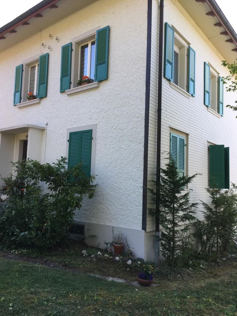 2-story house with white exterior walls, green shutters, and a small garden in the front.