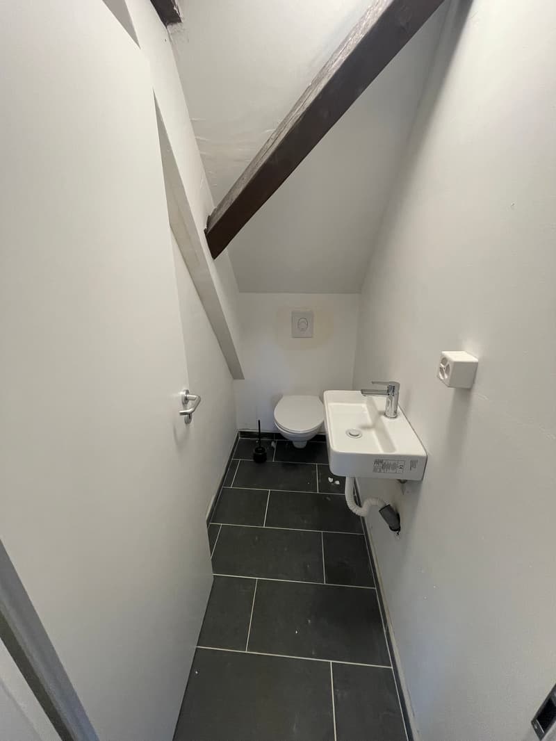 Small bathroom with white walls, black tile floor, toilet, and a small sink vanity.