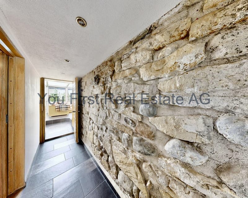 Authentischer Flurbereich mit rustikaler Natursteinwand und modernem Deckenfinish