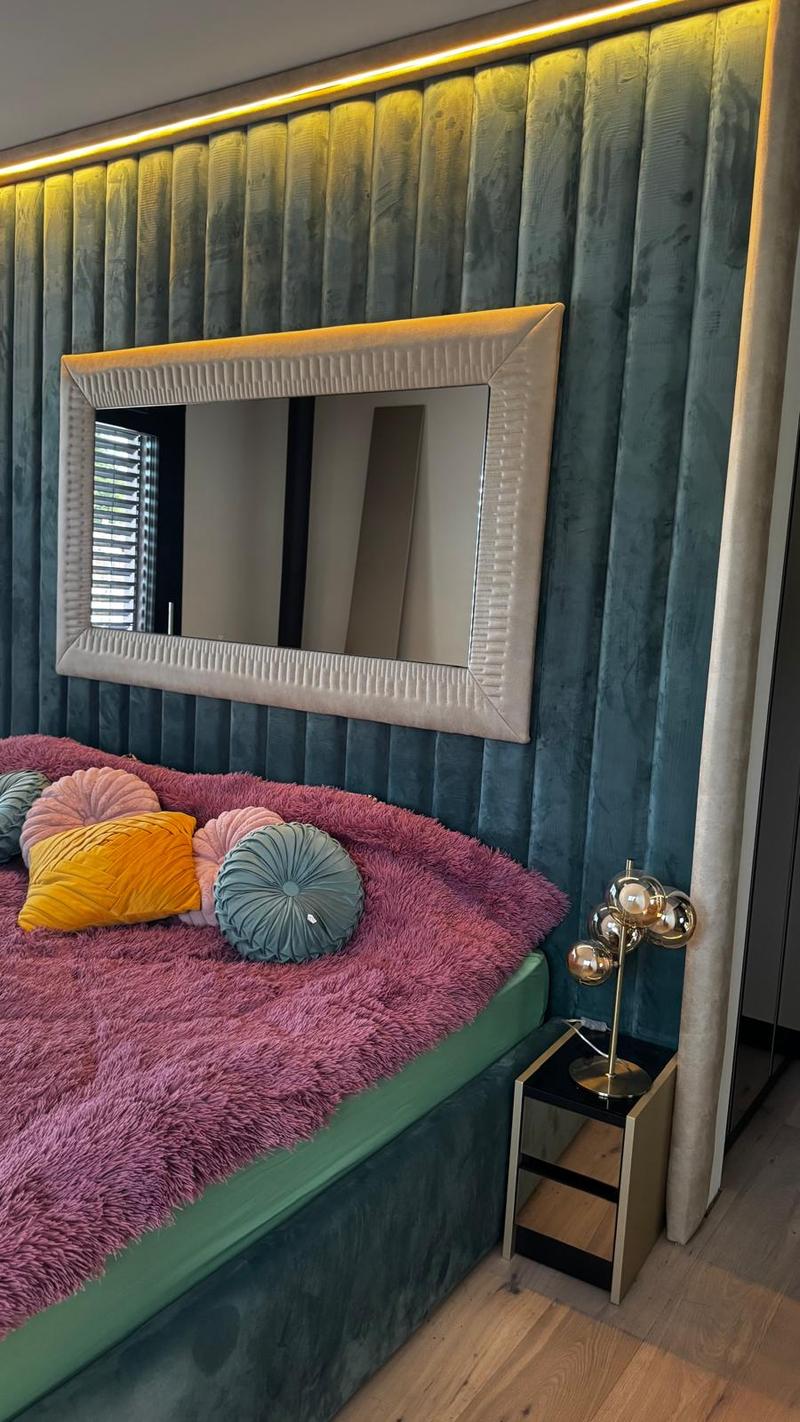 A wall covered in vertical blue and white stripes, a bed with pink and green fabric, a lamp on a nightstand, and a large mirror with a silver frame.
