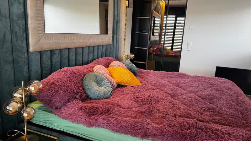 Large bed with pink fur, green blanket, large colorful pillows, large mirror, modern design