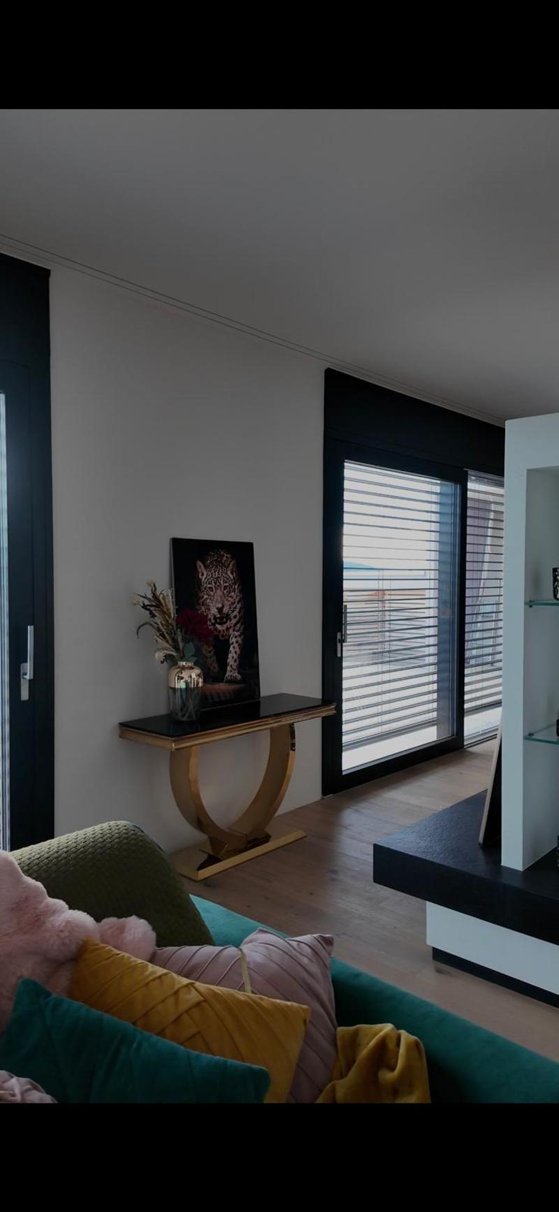 open room with sofa, decorative items, a table with a flower vase, balcony with glass door
