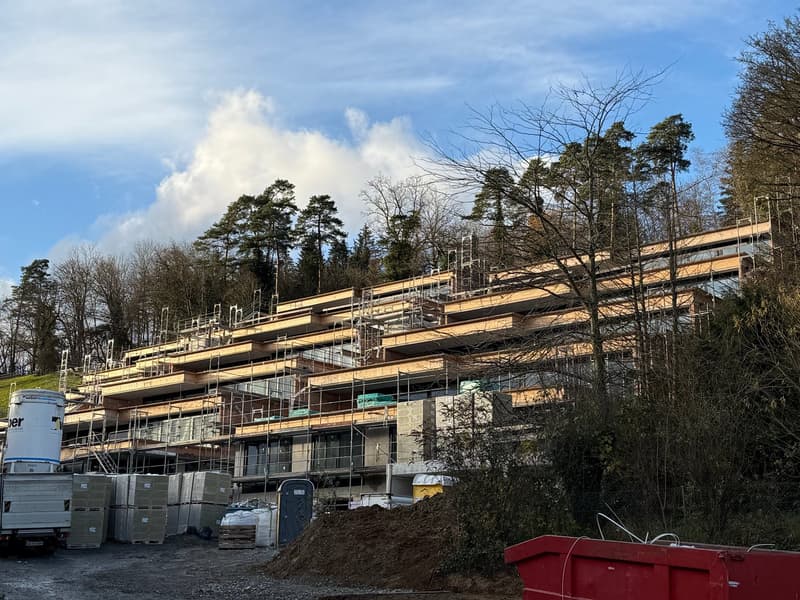 Building with multiple floors, currently under construction, visible scaffolding, situated on a hill
