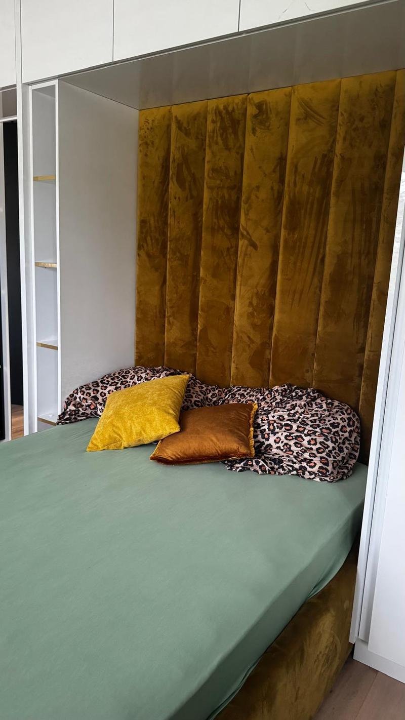 a cozy bedroom with a bed, velvet upholstered headboard, two pillows, wardrobe with shelves, wooden floor