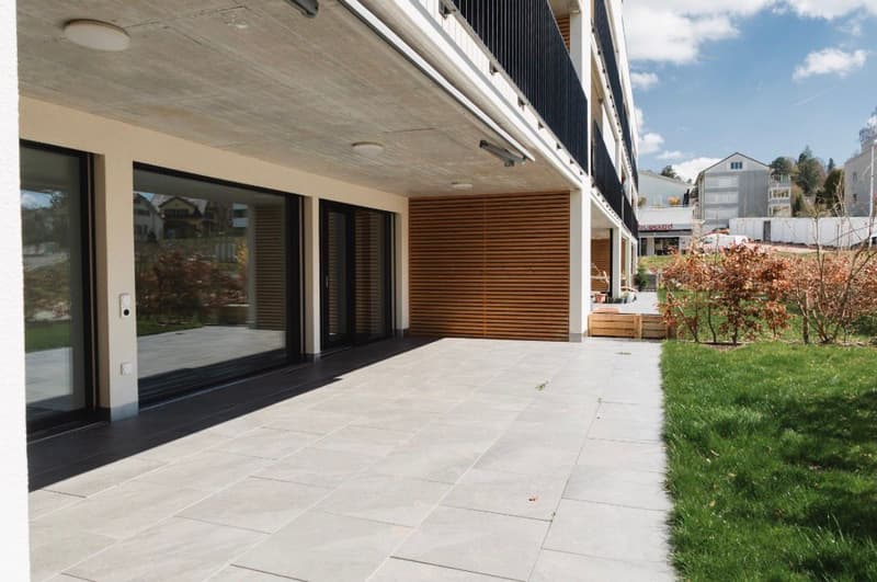 Modern building with large glass windows, wooden door, tiled floor, and a small garden area