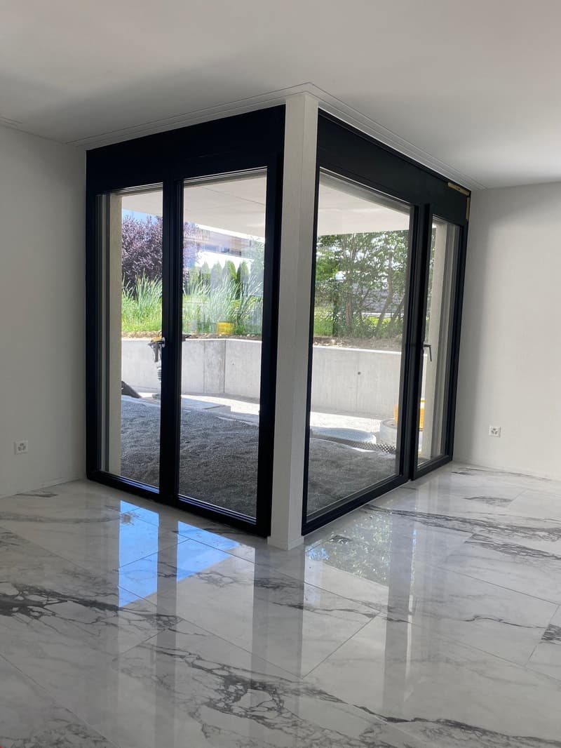 Large windows with black frames, marble flooring, white walls