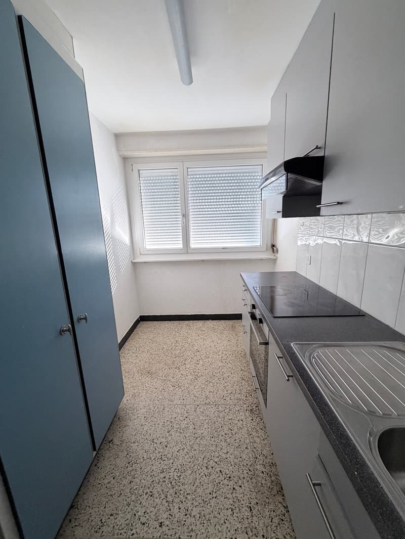 Empty kitchen with granite countertops, black stove, white cabinets, window with blinds, and a sink