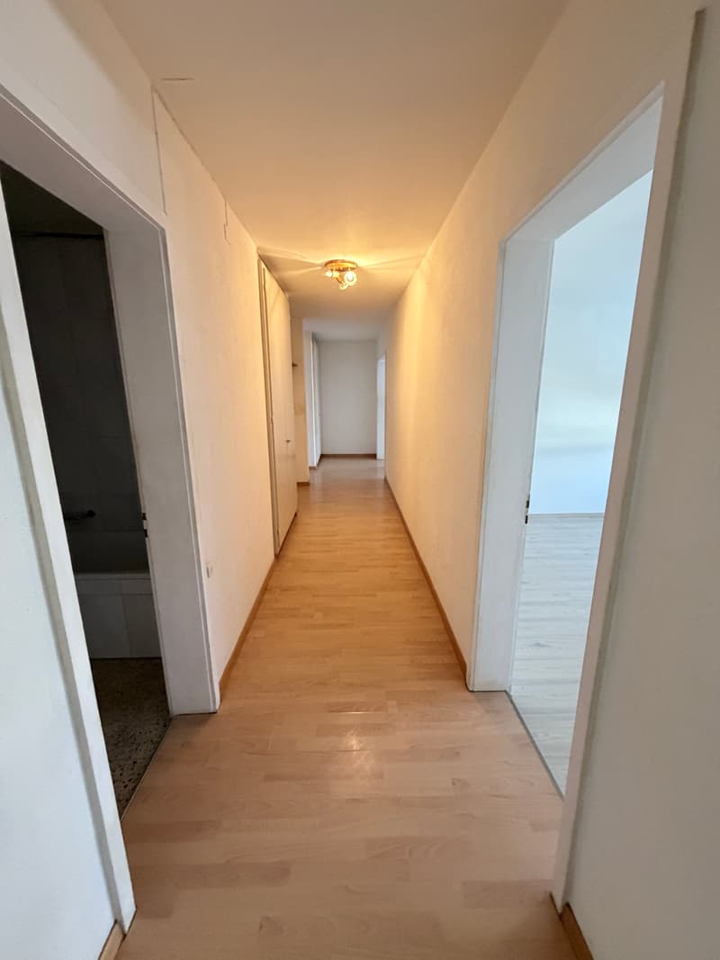 Empty hallway with wooden floors, white walls, and a ceiling light.