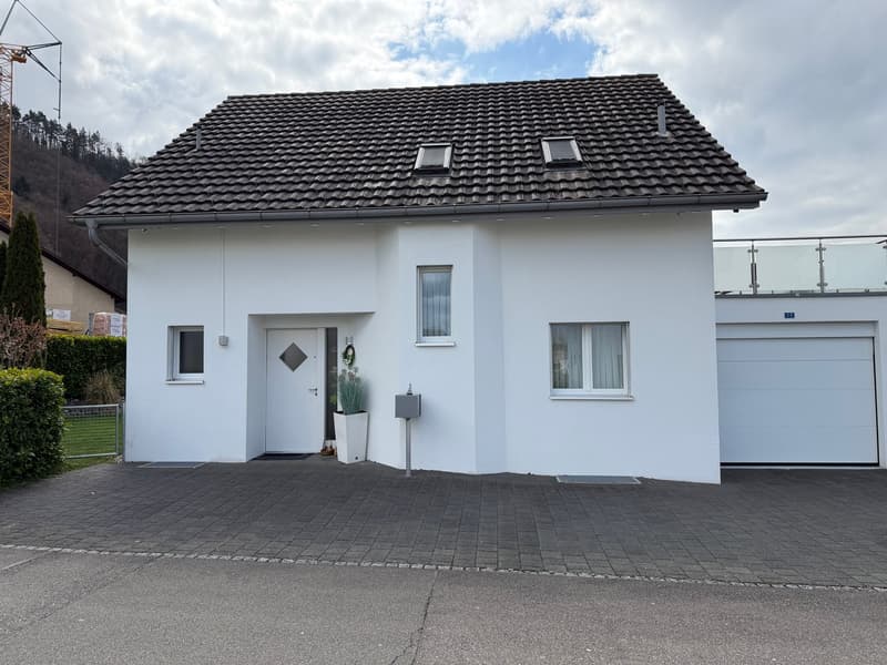 white house, brown roof, 2 garages, paved driveway, plants, windows, door