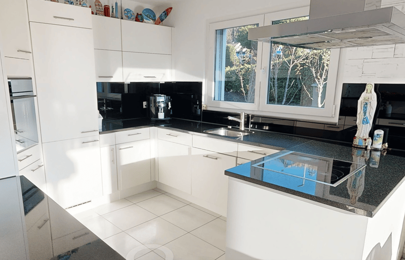 modern kitchen with white cabinetry, black granite countertops, modern appliances, stainless steel faucet, windows overlooking trees