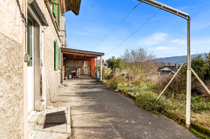 stone building with an entrance, garage, paved driveway, shrubs and trees in the garden, mountain view