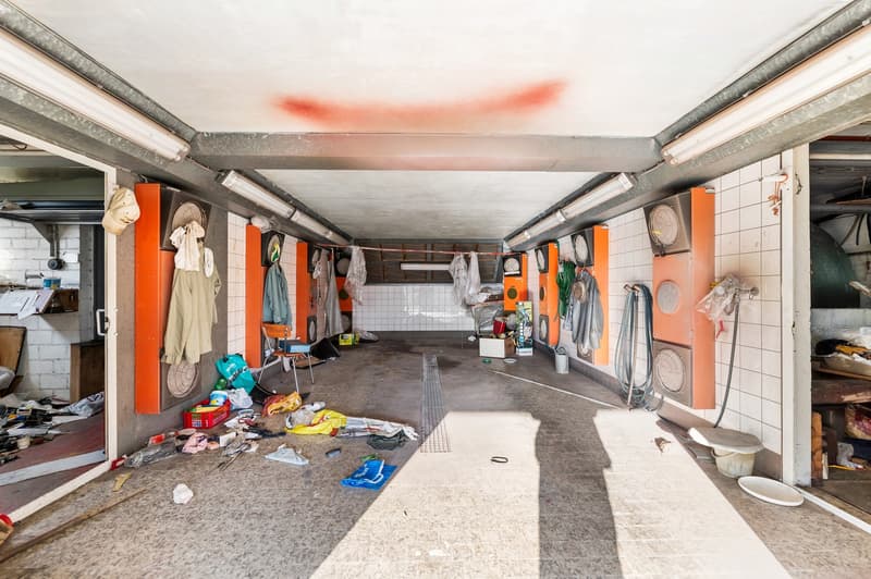 Concrete floor, multiple storage boxes, hanging tools, lamps attached to ceiling, scattered items