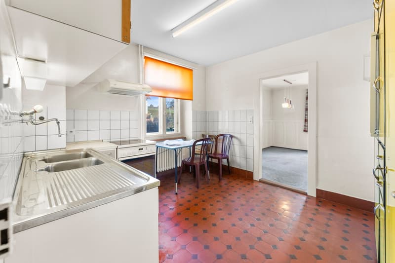 Kitchen with a sink, stove, and refrigerator in a corner, and a dining table with chairs by the window.