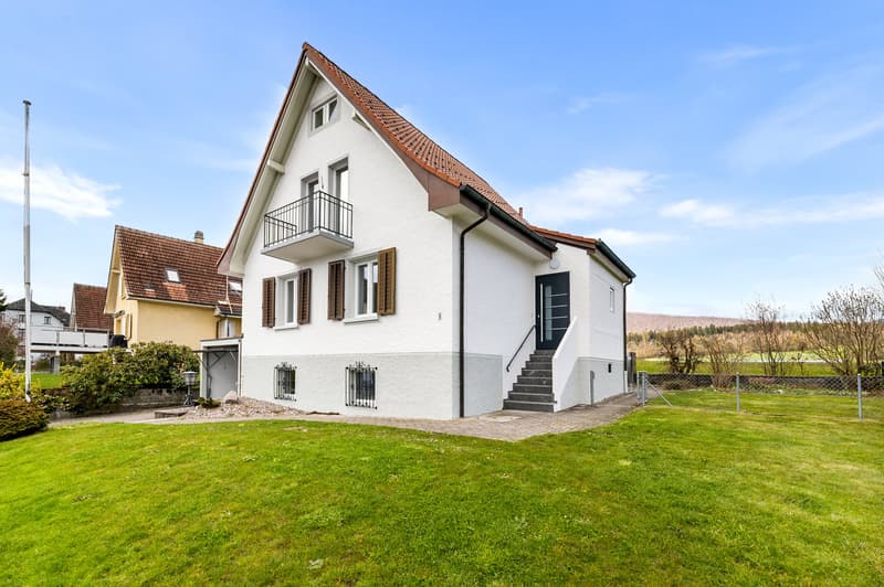 2 story house, white exterior, brown roof, balcony, fenced yard, green lawn
